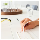 Hand connects white cord with plug to sleek, modern high table with cable management.