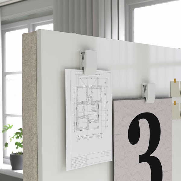 White office partition screen with attached diagram and hooks, divided into two sections, placed near a window with a plant.