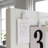 White office partition screen with attached diagram and hooks, divided into two sections, placed near a window with a plant.