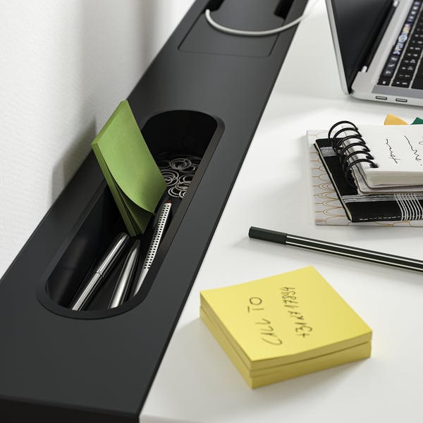 Black desk organiser with pens, paper clips, sticky notes, and notebook on white desk.