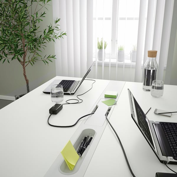 Modern office desk with integrated compartments. Three laptops, water bottles, and plants. Clean, organised workspace.