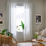 Living room with white curtains, plants, wicker chair, art, couch, and rug.