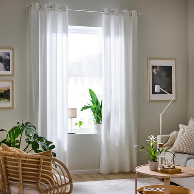Living room with white curtains, plants, wicker chair, art, couch, and rug.