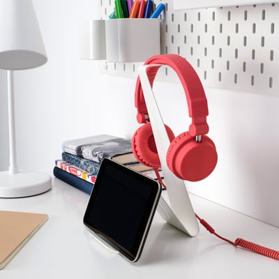 Small red headphones stand on desk with tablet, next to books and lamp. Epoxy-coated steel, v shape, fits neatly among items.