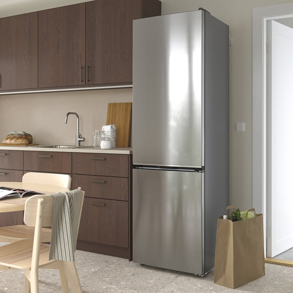Modern kitchen with stainless steel MÖLNÅS fridge freezer, wooden chair, bread, and grocery bag near door.