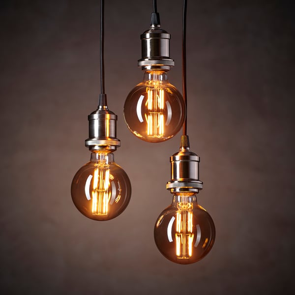 Three vintage-style light bulbs with silver bases hang against a dark background, emitting warm, yellowish light.