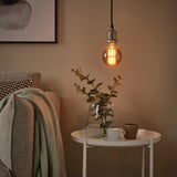 Cozy corner with hanging bulb, side table, blanket, and eucalyptus vase.