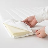 Person opening NÄSFJÄLLET mattress pad, showing soft foam for comfort.
