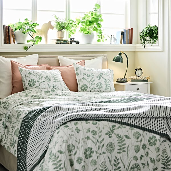 A green and white NÅLBJÖRNBÄR duvet set with floral prints, cotton-viscose blend for comfort. Bedside table with lamp and clock.