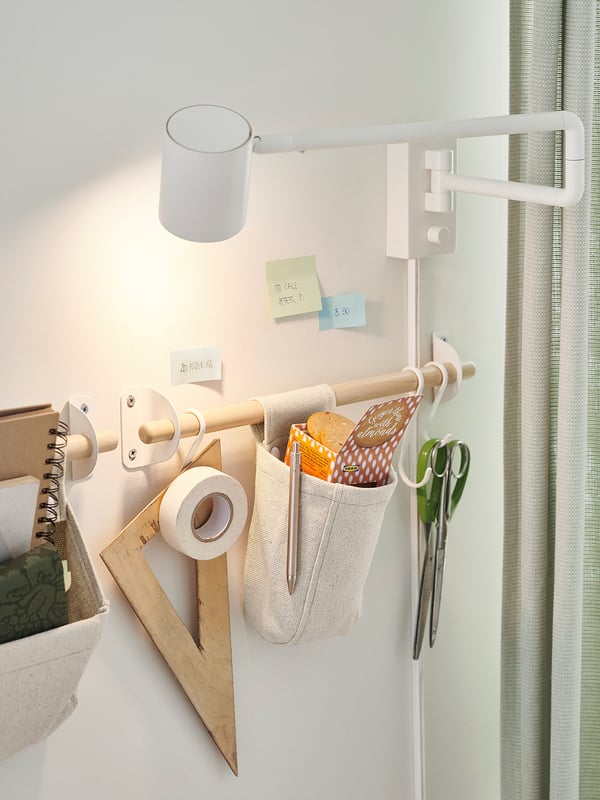 Office supplies in beige pouch and wooden box, sticky notes, and lamp on white rail.