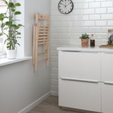 Modern kitchen with wooden foldable chair and white cabinets. A potted plant and clock on the white tiled backsplash.