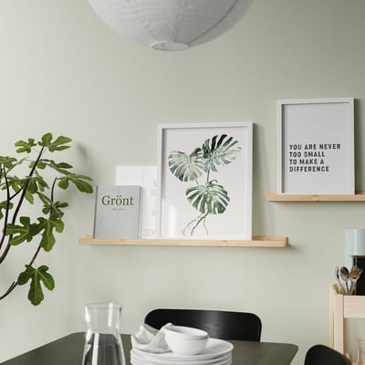A modern dining room a wooden shelf displaying framed art, books, and a plant. A table set with cups and plates is set below.