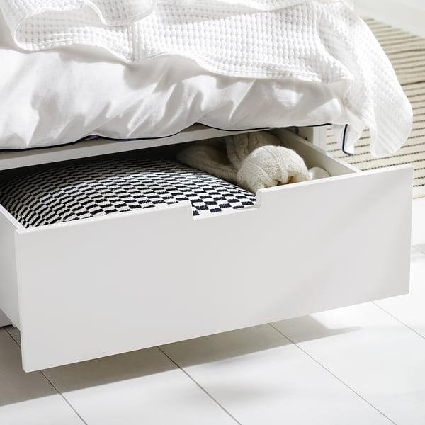 White underbed drawer open, storage unit with knitted hat, folded blanket, black and white patterned sheet.
