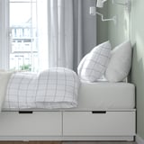 White NORDLI bed with 6 drawers visible, plus white grid bedding and pillows.