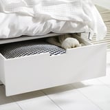 Open white bed drawer with blanket, socks, and black patterned sheet.