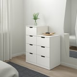 Minimalist white dresser with six drawers, plant, and bowl in bedroom, mirror reflects room.