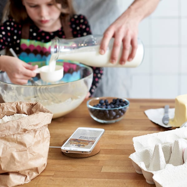 Two people cooking; one pours milk into bowl, phone with recipe nearby.