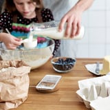 Two people cooking; one pours milk into bowl, phone with recipe nearby.