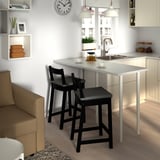 Modern kitchen with white counters, sink, large window, and NORDVIKEN stools. Shelves and clock complete the space.