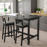 Modern kitchen with black NORDVIKEN bar table and stools, cushioned seats, near window with plants and teapot.