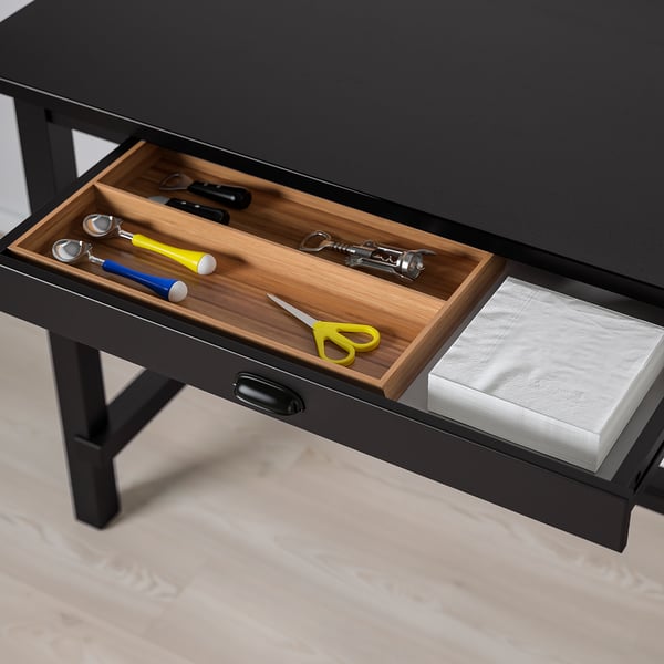 Black bar table drawer with wooden tray holding kitchen tools and a stack of white napkins.