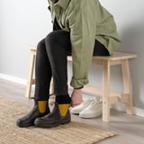 Two people sitting on wood online bench, one wearing black boots, the other white sneakers.