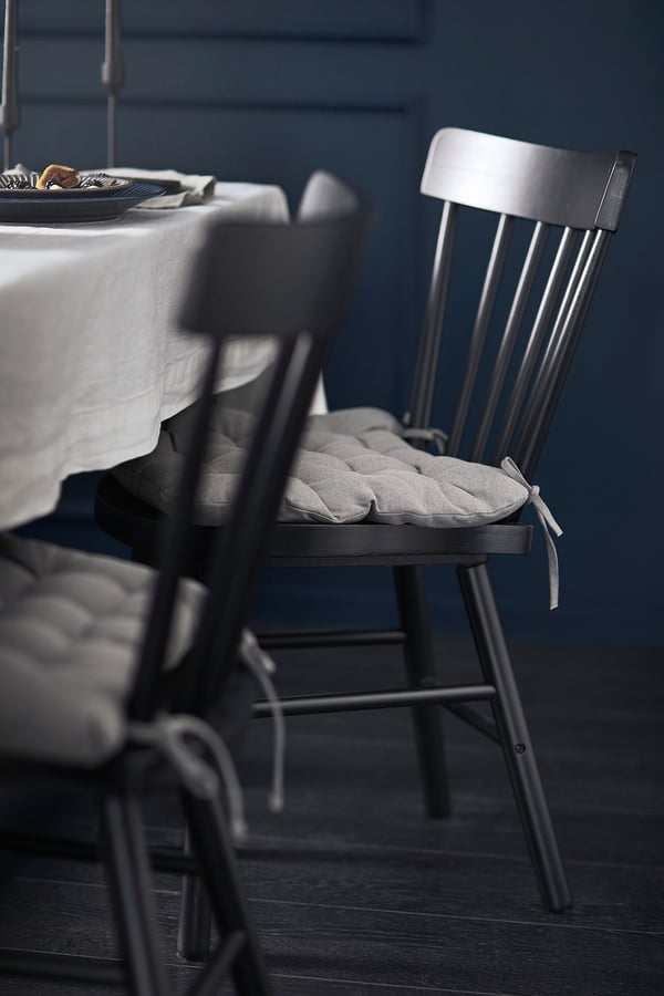 Black spindle dining chair with cushioned seat and curved back, set against dark blue wall.