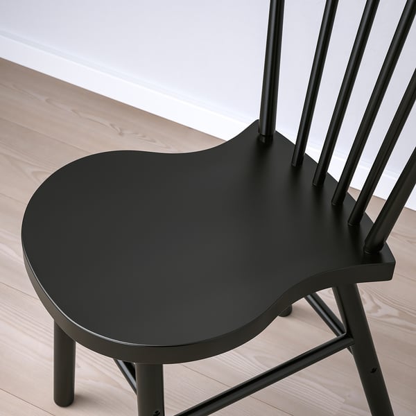Black painted wooden chair on light wooden floor; focus on back support.
