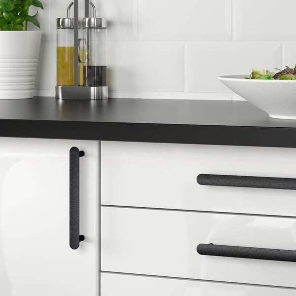 Modern kitchen with white drawers and black handles, holding a bowl of salad, plates, bottles, and a plant.