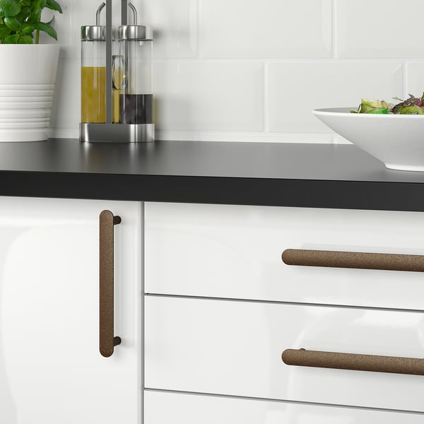 Modern kitchen with white cabinets and black countertop, featuring cork-handled drawers. A bowl of salad and oil dispenser are placed on the counter.