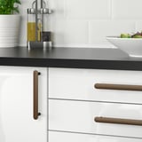 Modern kitchen with white cabinets and black countertop, featuring cork-handled drawers. A bowl of salad and oil dispenser are placed on the counter.
