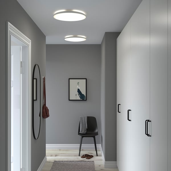 A modern entryway with NYMÅNE ceiling lights providing ample light. The hallway has gray walls, a black chair, and a round mirror.