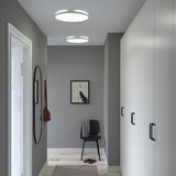 A modern entryway with NYMÅNE ceiling lights providing ample light. The hallway has gray walls, a black chair, and a round mirror.