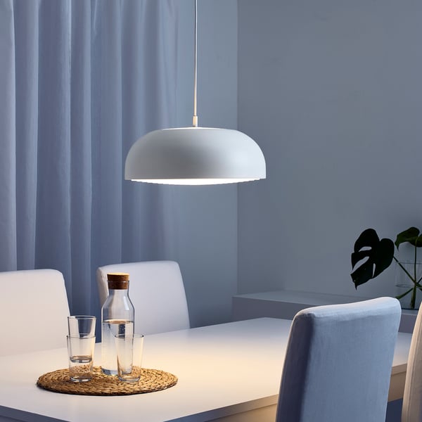 Modern dining area with white chairs around a table under a pendant lamp. A water carafe and glasses are on the table.