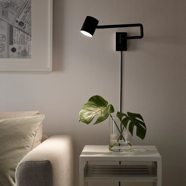 Bedside adjustable lamp NYMÅNE illuminates over a plant, providing directed light.