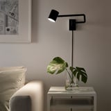 Bedside adjustable lamp NYMÅNE illuminates over a plant, providing directed light.