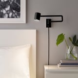 Bedside black wall lamp, adjustable & dimmable, illuminating white pillow area, near green plant & books.