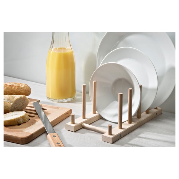 Wooden dish rack with dowels holding white plates. Orange juice and bread nearby.