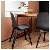 Modern dining setup with two dark grey ODGER chairs and a wooden table, featuring a stylish, curved design with a textured finish.