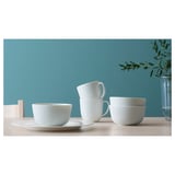 White porcelain dinner set: cups, bowls, and plates with vertical ribbed design against teal wall.