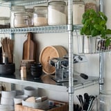 Modern metallic kitchen shelf with jars of ingredients and baskets.