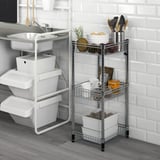 Kitchen setup with small chrome OMAR storage rack. Holds fruit, utensils, and mugs near sink. Adjacent white cart has stacked bins.
