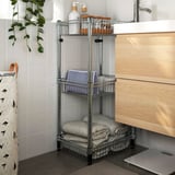 OMAR silver metal storage rack with towels and bottles. Sleek, tall, fits under wood cabinet, adds bathroom storage.