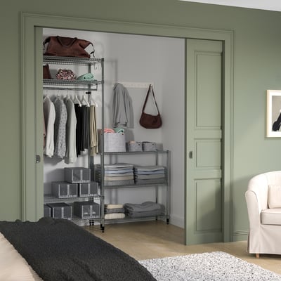 Green OMAR shelving with adjustable metal racks, neat clothes, and bags in a cozy green room.