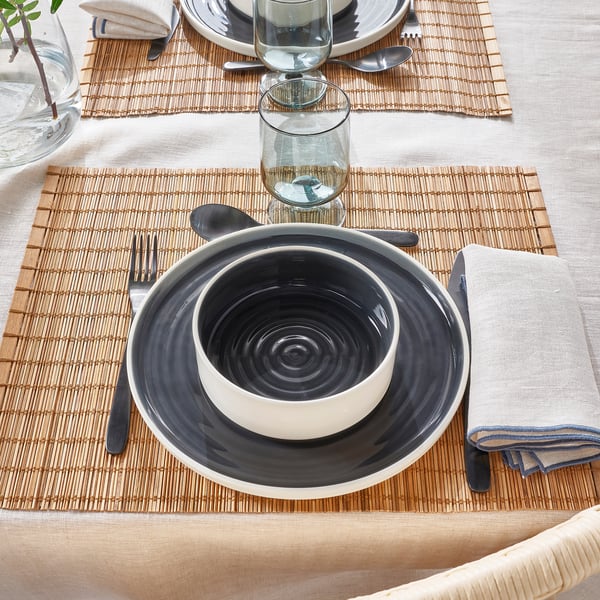 Table setting with gray ceramic bowl on white plate, glass, and cutlery.