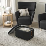 Two dark grey upholstered chairs with wooden legs; one has a matching footstool with open storage for a blanket.