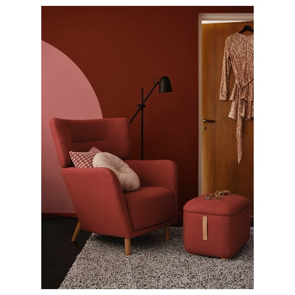 Modern red chair with wood legs, matching footstool, lamp, cozy corner.