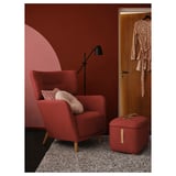 Modern red chair with wood legs, matching footstool, lamp, cozy corner.