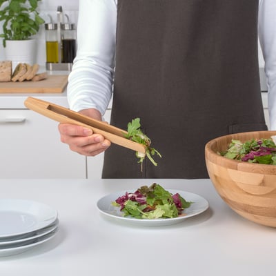Person using bamboo tongs to serve salad from a bowl onto a plate. The tongs are effectively picking out specific salad ingredients.