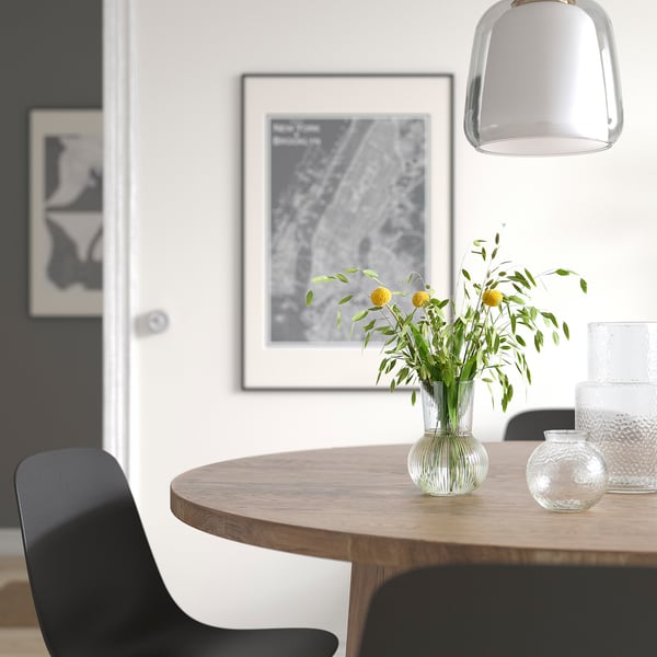 Modern dining area with round table, black chairs, yellow flowers in glass vase, pendant lamp, art on wall.
